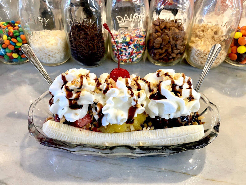 A banana split in a long dish, with the jars of toppings lined up behind it.