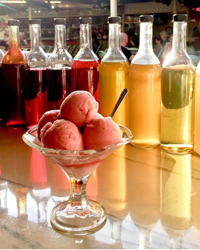 A coupe of pink scoops with the syrup bottles behind.