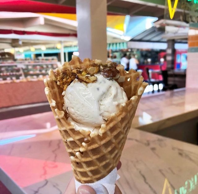 A waffle cone with a pale scoop, the market stalls behind.