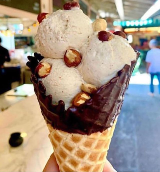 A chocolate dipped waffle cone with hazelnuts, held up in the market.