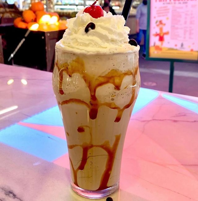 A tall shake with caramel sauce and a cherry.