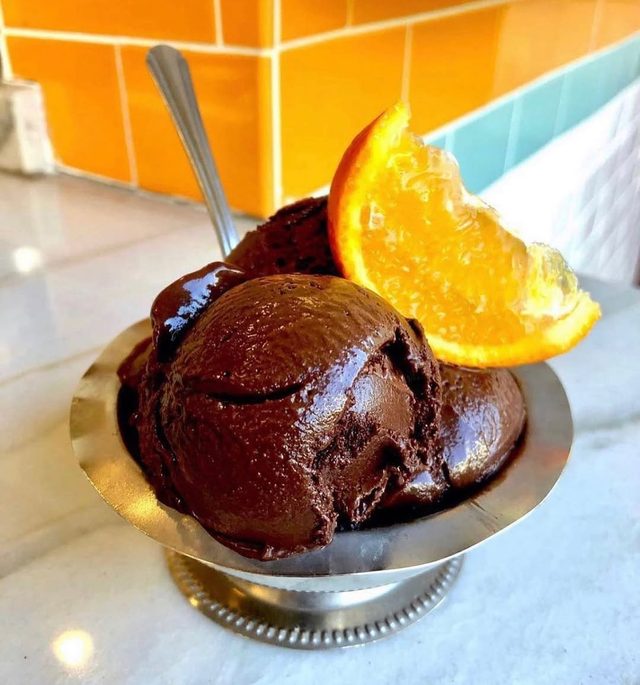 A silver dish of dark chocolate scoops with a slice of orange.