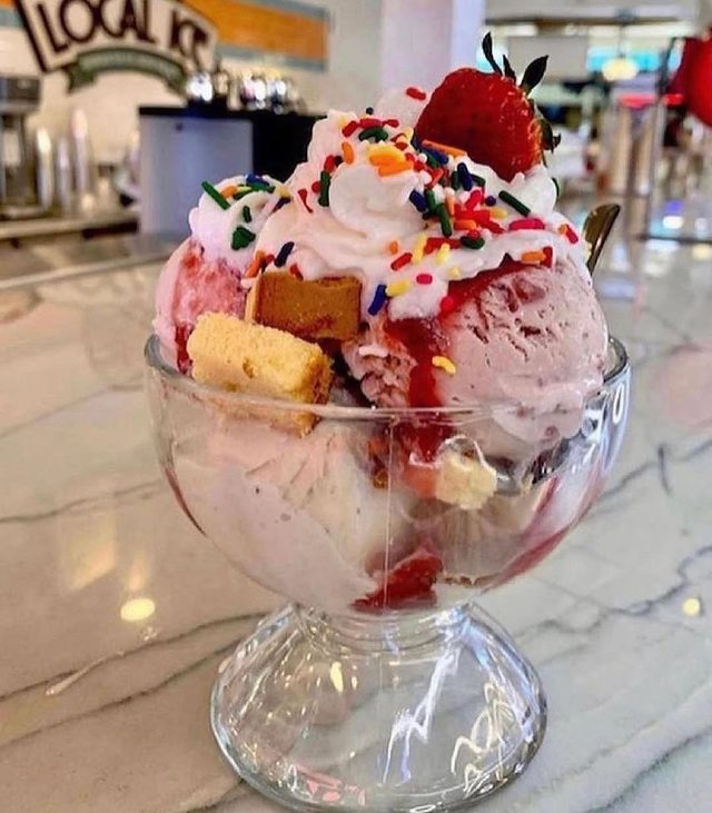A tall sundae with strawberry and sprinkles.