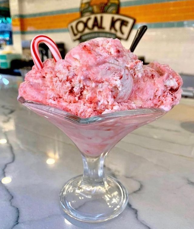 A coupe of pink scoops on the marble counter with a candy cane.