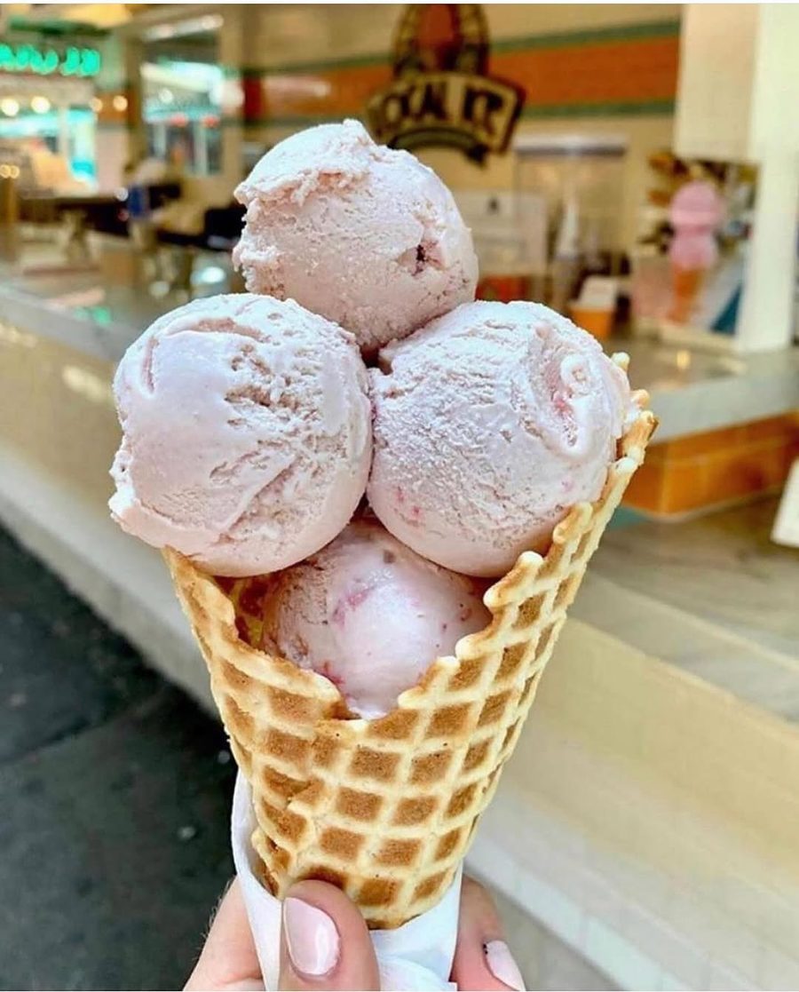 A waffle cone with three pale pink scoops, held up at the counter.