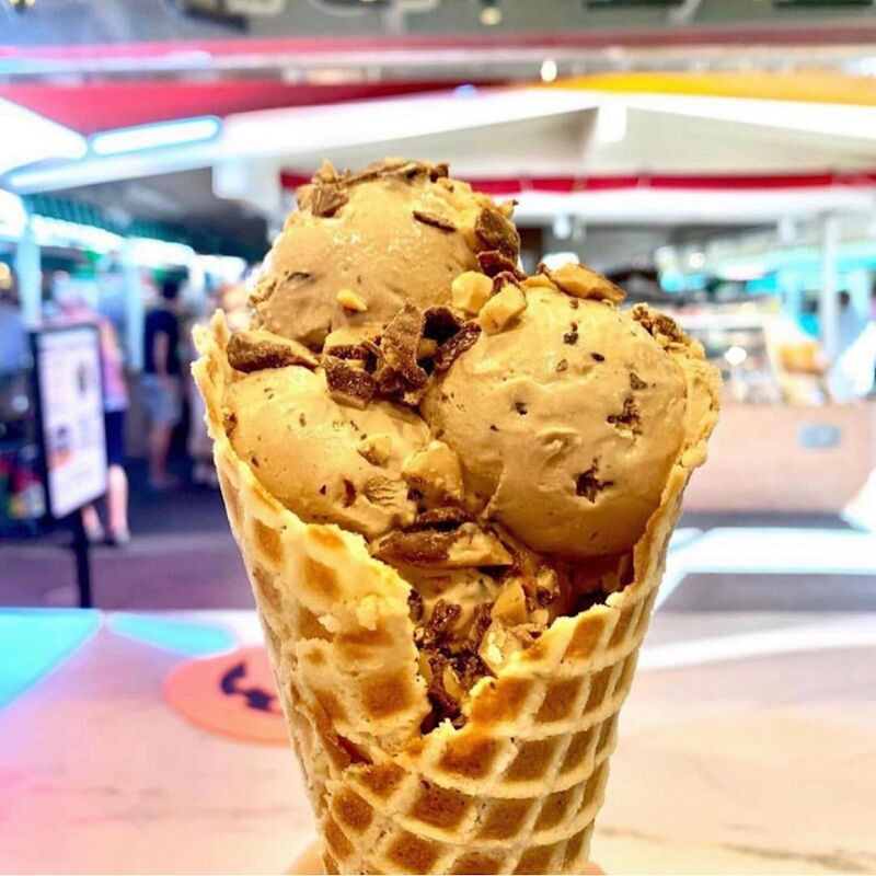A waffle cone with two scoops, held up in the market.