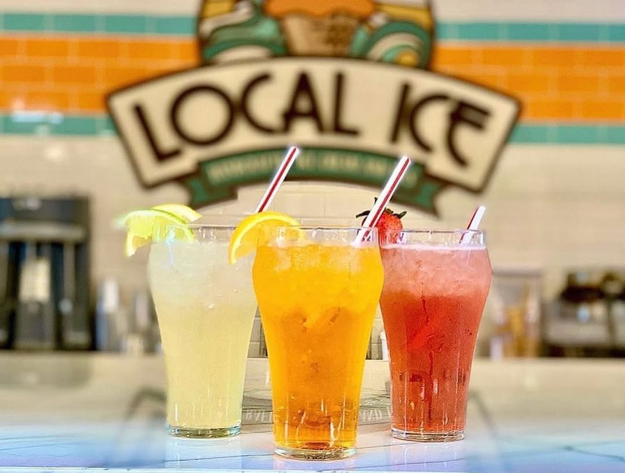 Three tall glasses of Italian soda, yellow, orange and red, under the Local Ice sign.