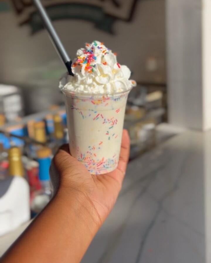 A hand holding a cup of ice cream topped with whipped cream and sprinkles.