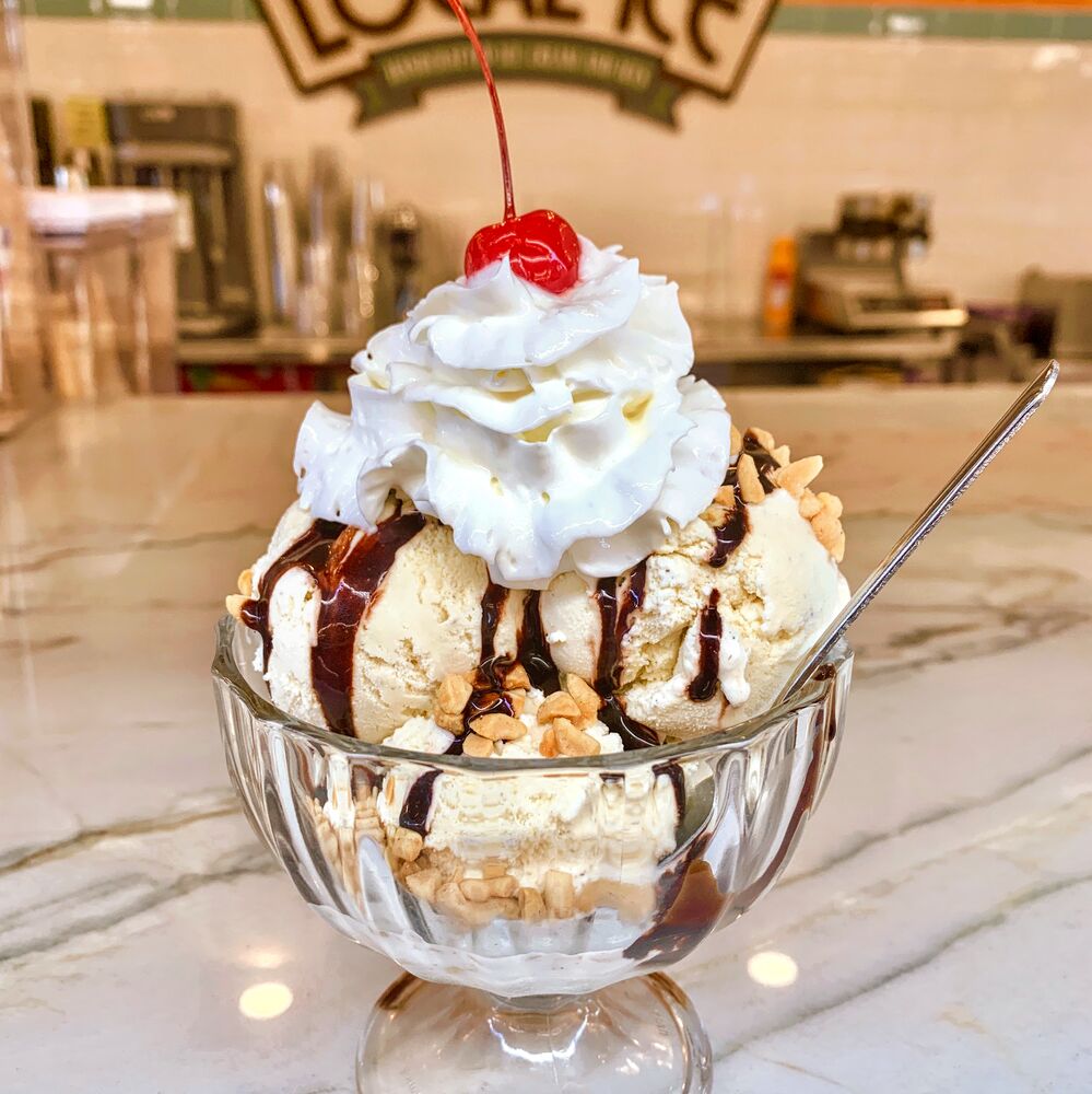 A sundae in a footed glass with whipped cream, chocolate sauce, nuts and a cherry.