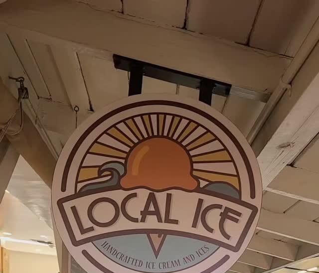 The round Local Ice sign hanging from the market's wooden ceiling above the counter.